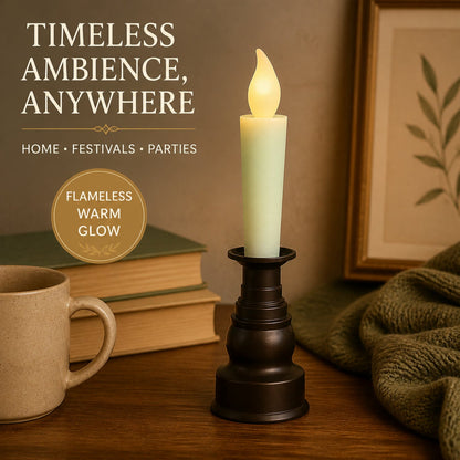 A cream LED candle with a flickering flame in a dark bronze holder, with a mug, books, and framed art.