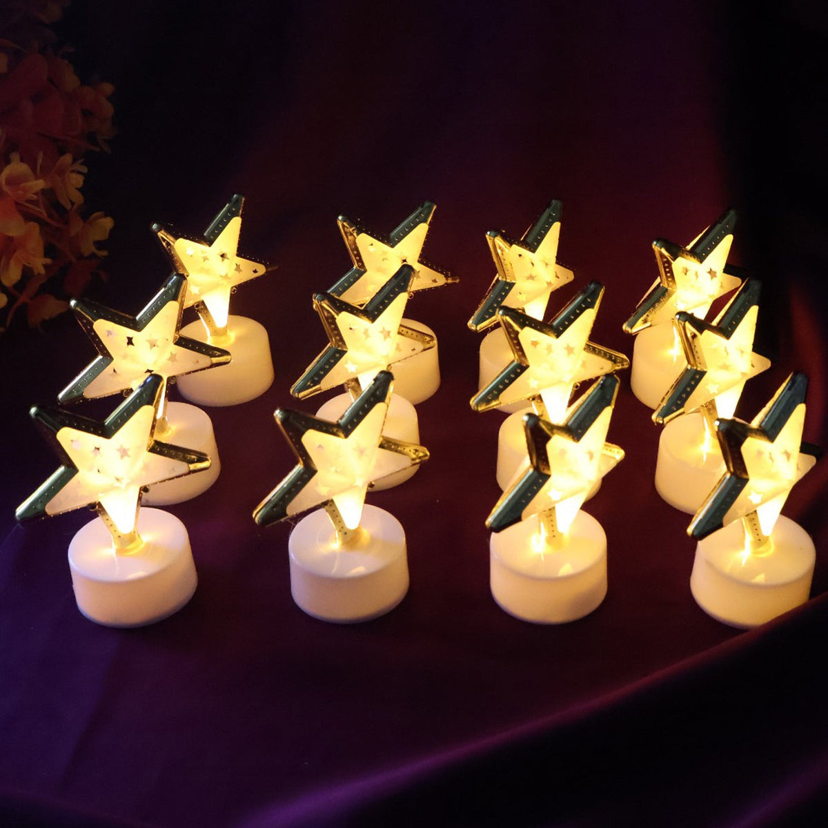 Twelve glowing star-shaped LED candles with gold frames and white bases arranged on a dark purple fabric.