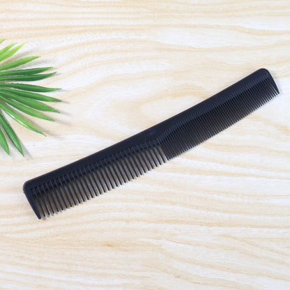 A black dual-tooth comb rests on a light wood surface, with a green leaf in the background.