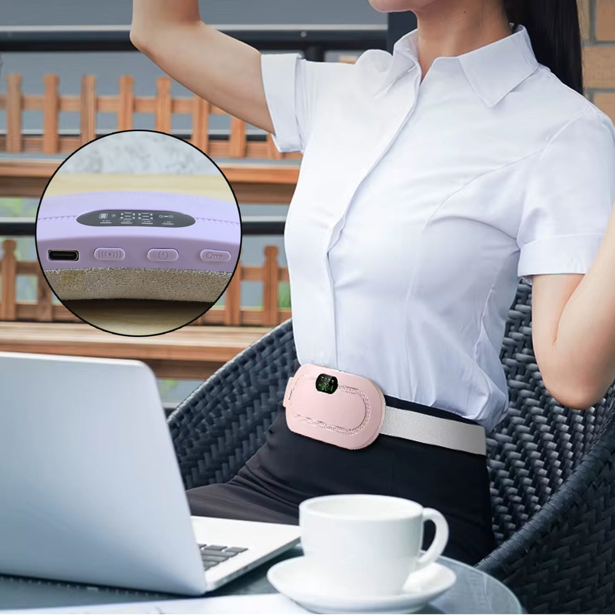 A woman sitting at a table with a laptop and coffee, wearing a pink heating pad on her lower abdomen.