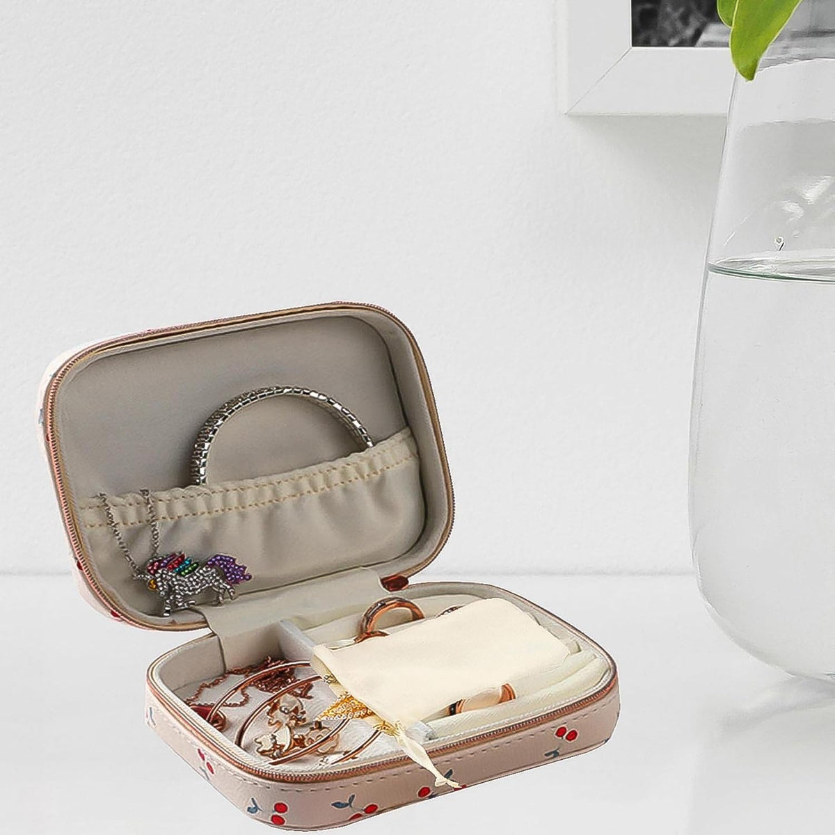 An open cherry print jewelry organizer case with a bracelet, necklace, rings, and a small bag on a table.