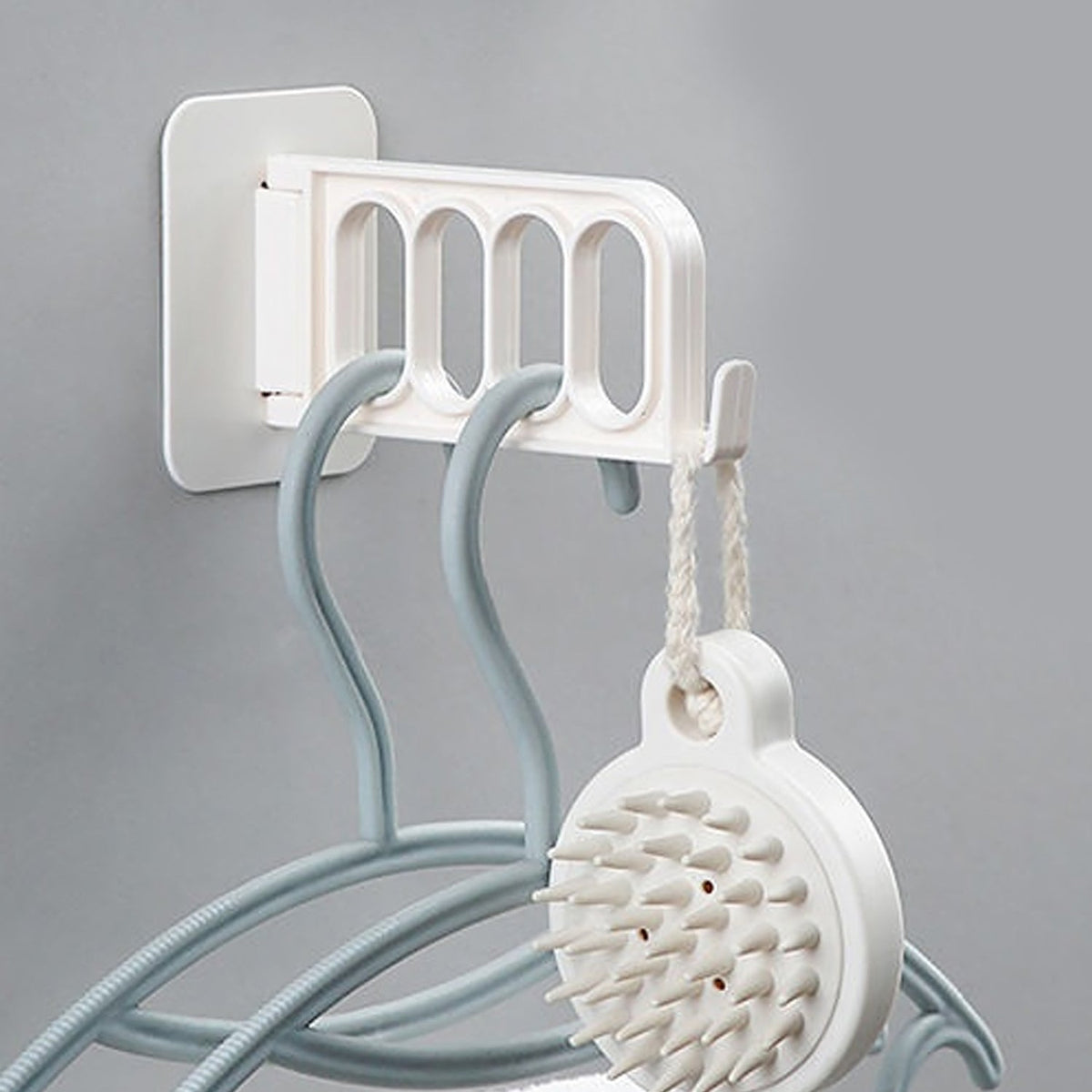 A white foldable wall hook holds a white scalp massager and two blue hangers with clothes.