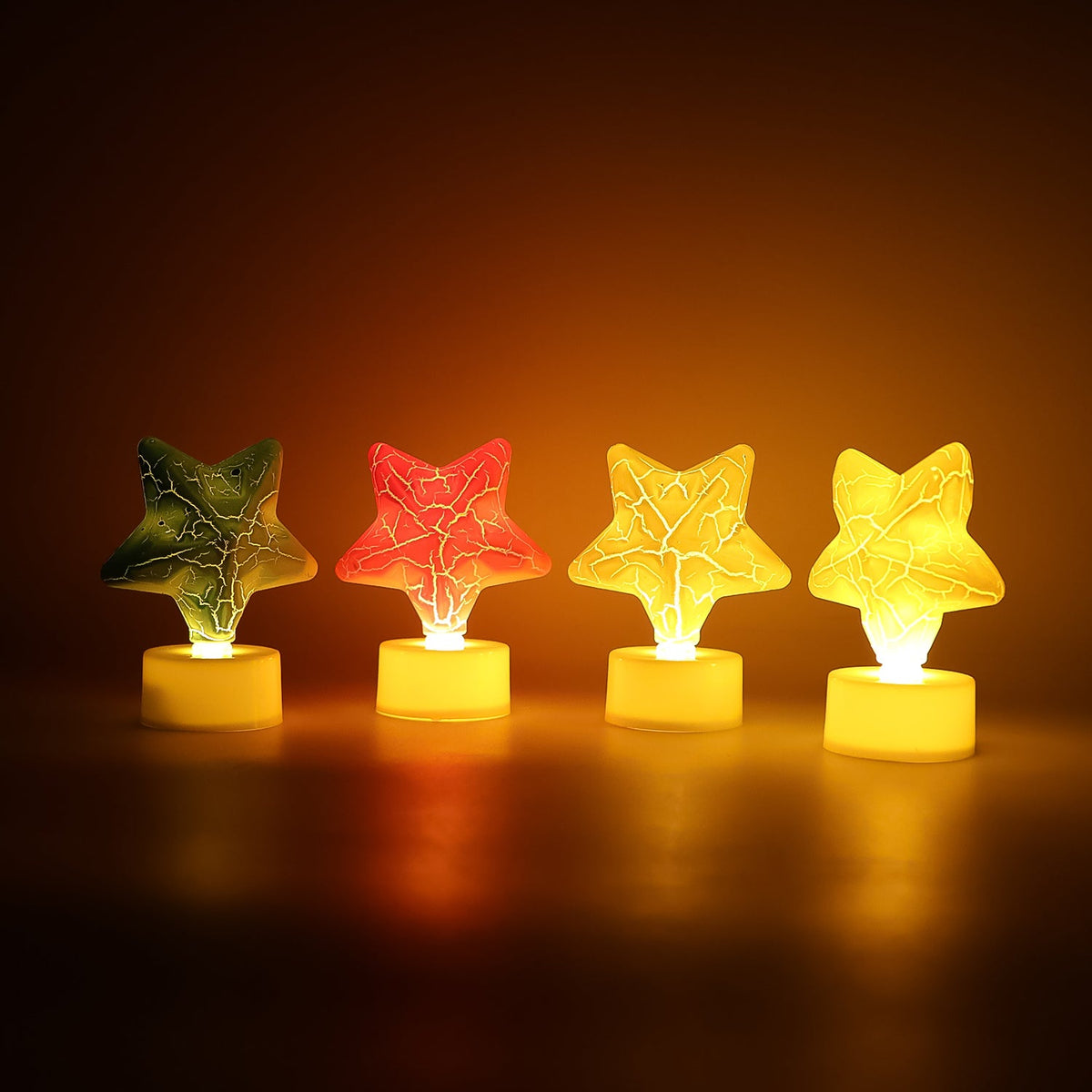 Four glowing star-shaped LED tealight candles in green, red, and two yellow, arranged in a row in a dark setting.
