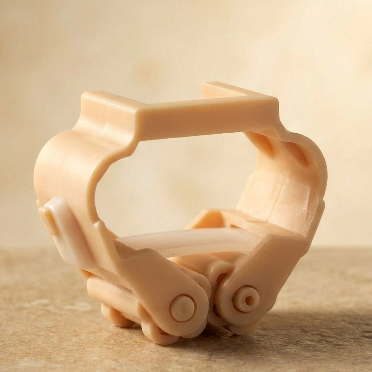 A peach-colored plastic broom holder with a hinged, gripping mechanism is shown on a light brown surface.