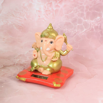 A Ganesha idol on a red base with gold accents, placed on a pink marble-patterned surface.