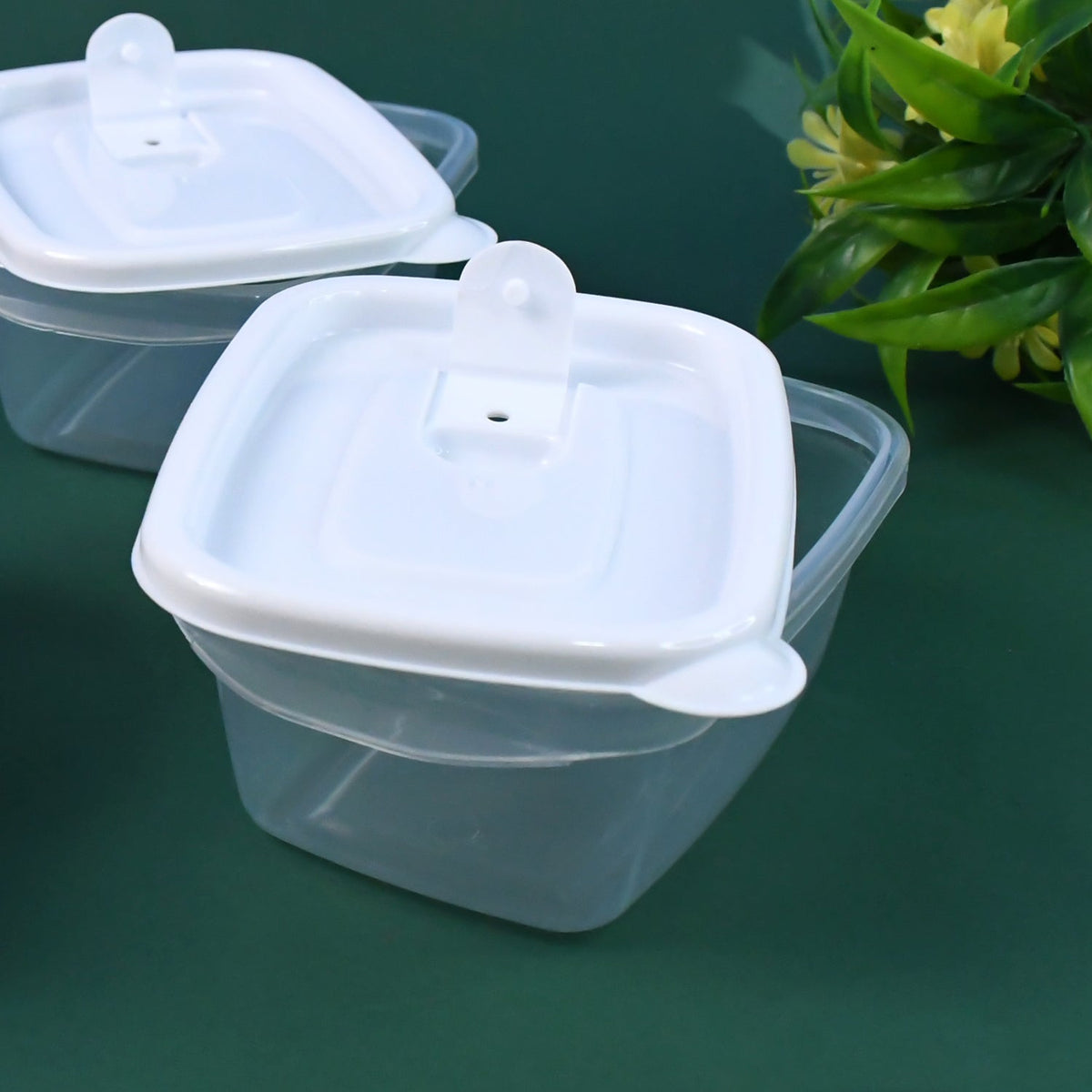 Close-up of a single clear plastic food container with a white lid and a small handle on a dark green surface.