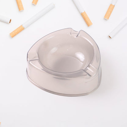 A purple transparent plastic ashtray is on a wooden table with pipes, a lighter, and pipe cleaning tools.