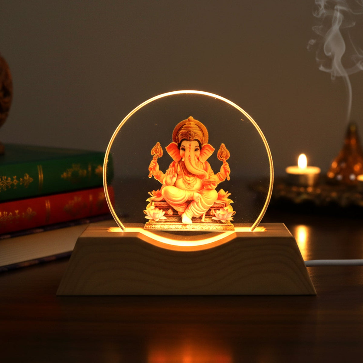 Lord Ganesha LED lamp with a golden glow on a dark table with books and a lit candle.