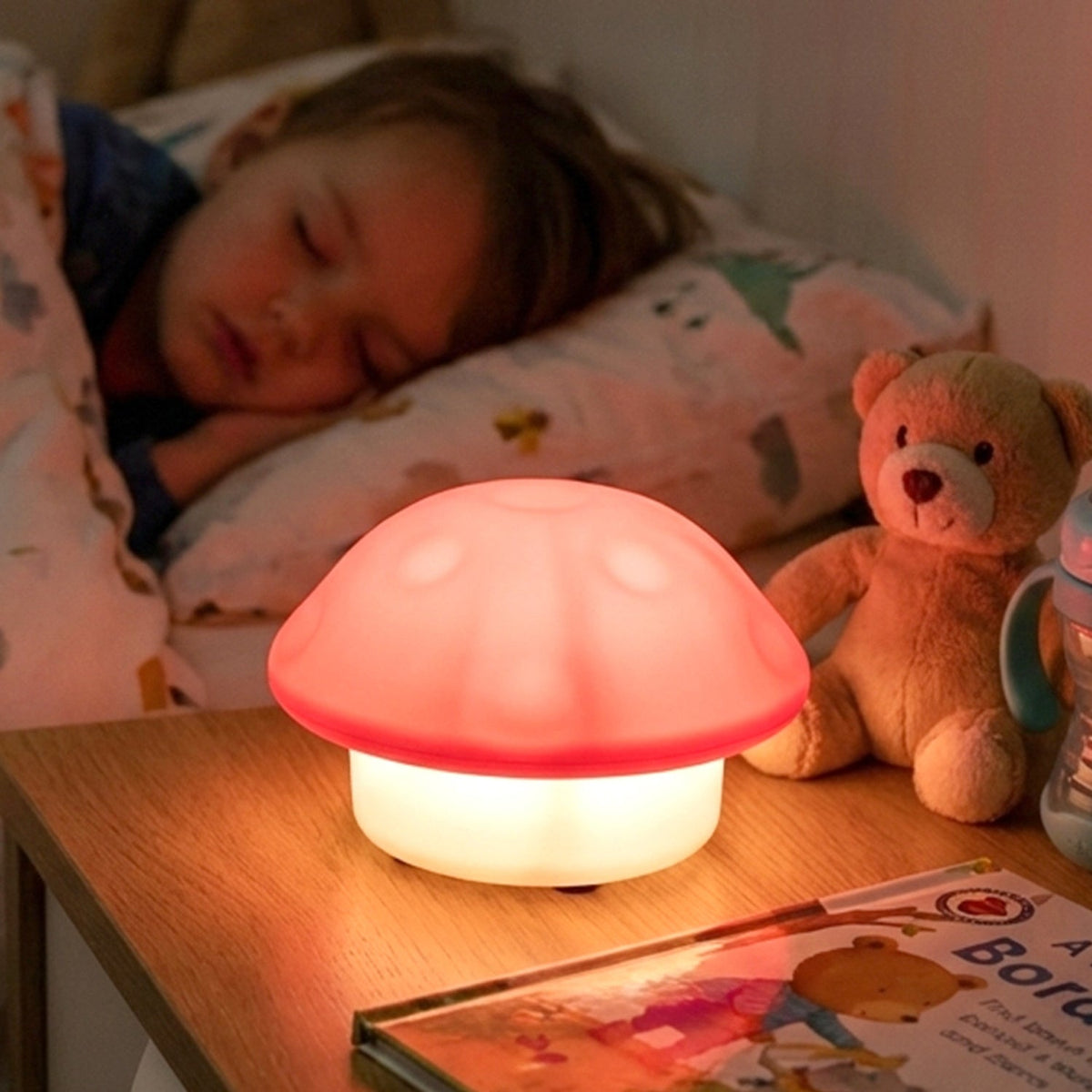 Glowing mushroom night light on a bedside table with a sleeping child and teddy bear.