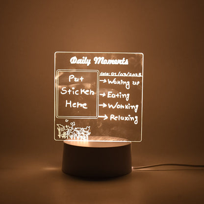 A softly glowing acrylic message board lamp on a dark surface, displaying a daily schedule.
