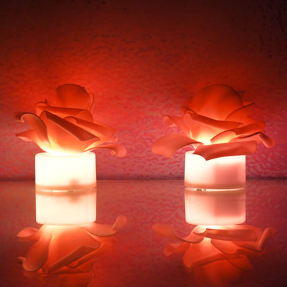 Two glowing orange LED rose tea lights reflected on a surface against a textured red background.