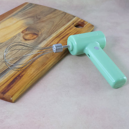 Light green cordless electric whisk with its attachment resting on a brown counter next to a wooden cutting board.