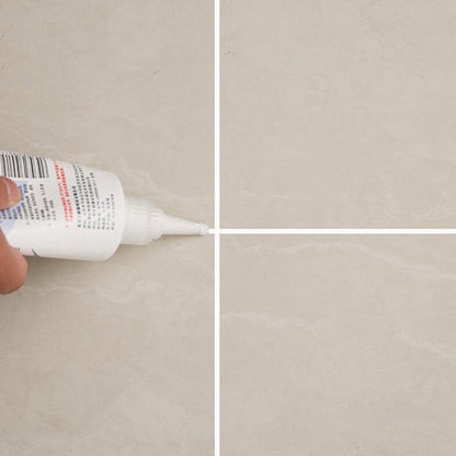 Close-up of a hand applying white sealant from a tube to the intersection of four beige floor tiles.
