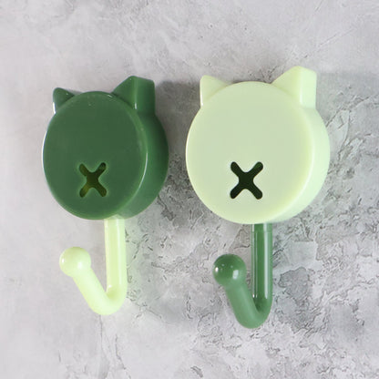 A close-up of two cat-shaped wall hooks, one dark green with a light green hook, and one light green with a dark green hook.