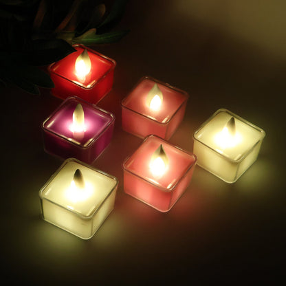 Six square LED flameless tealight candles glowing in yellow, red, and purple, arranged on a dark surface with a plant in the