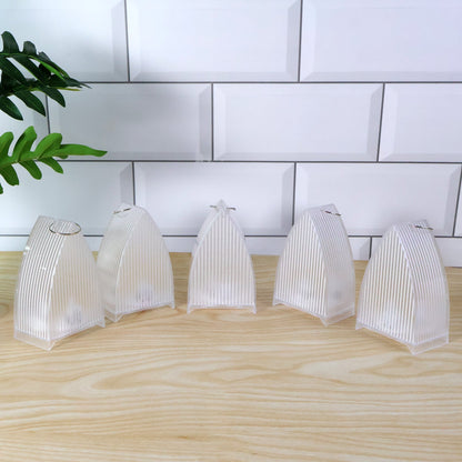 Five clear plastic ribbed lanterns with metal hooks on top, arranged on a light wooden surface against white subway tiles.