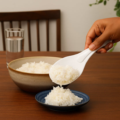 A hand scoops white rice from a brown bowl onto a small blue plate using a white rice paddle.