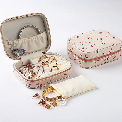 An open cherry print jewelry organizer with rings, bracelets, earrings, and a closed case with a pouch.