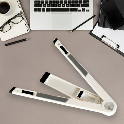 A white foldable stand, partially folded, rests on a gray desk with a laptop, notebook, and coffee.