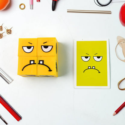 A yellow emotion cube displaying a sad face is next to a matching yellow card on a white surface with various office