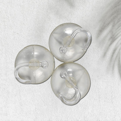 Three transparent suction cup hooks are arranged on a white textured surface with a subtle shadow.
