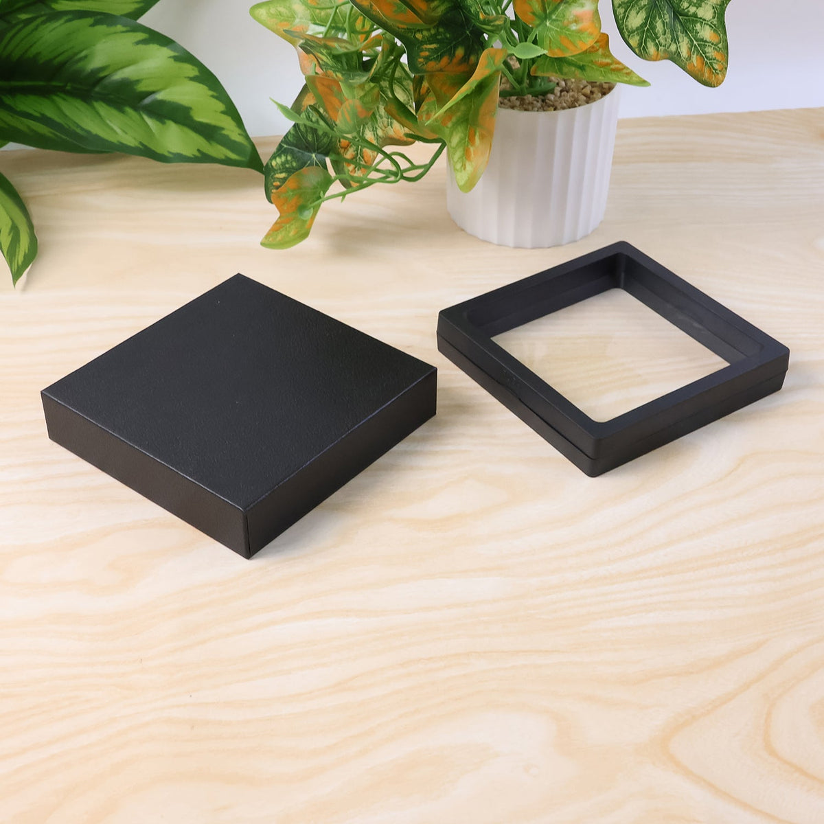 Two black square box pieces, one with a clear film and the other solid, on a wooden surface.