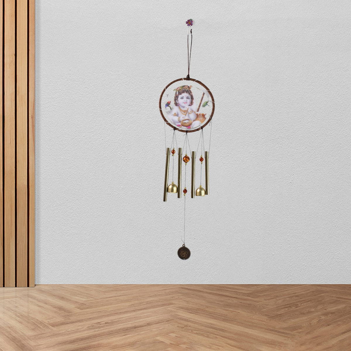 The Krishna wind chime hangs on a white wall, with a wooden panel on the left and a wooden floor below.
