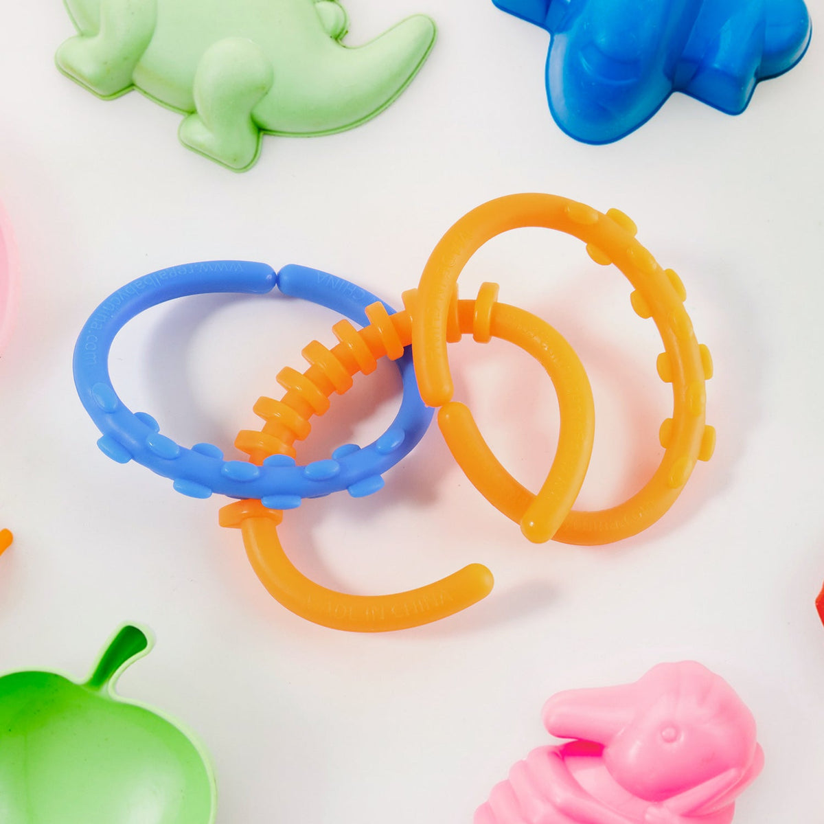 Three interconnected orange and blue learning links on a white surface, surrounded by colorful dinosaur-shaped toys.