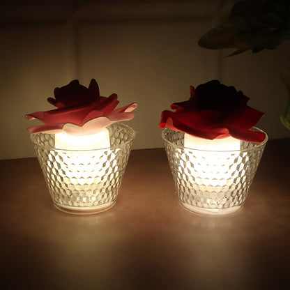 Two glowing rose-shaped LED candles, one red and one pink, in clear textured holders on a dark surface.