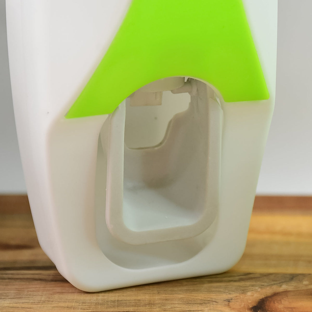 Close-up of the white and lime green automatic toothpaste dispenser showing the internal mechanism on a wooden surface.