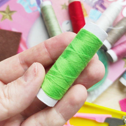 A hand holding a spool of bright green thread, with other colorful threads and sewing notions blurred in the background.