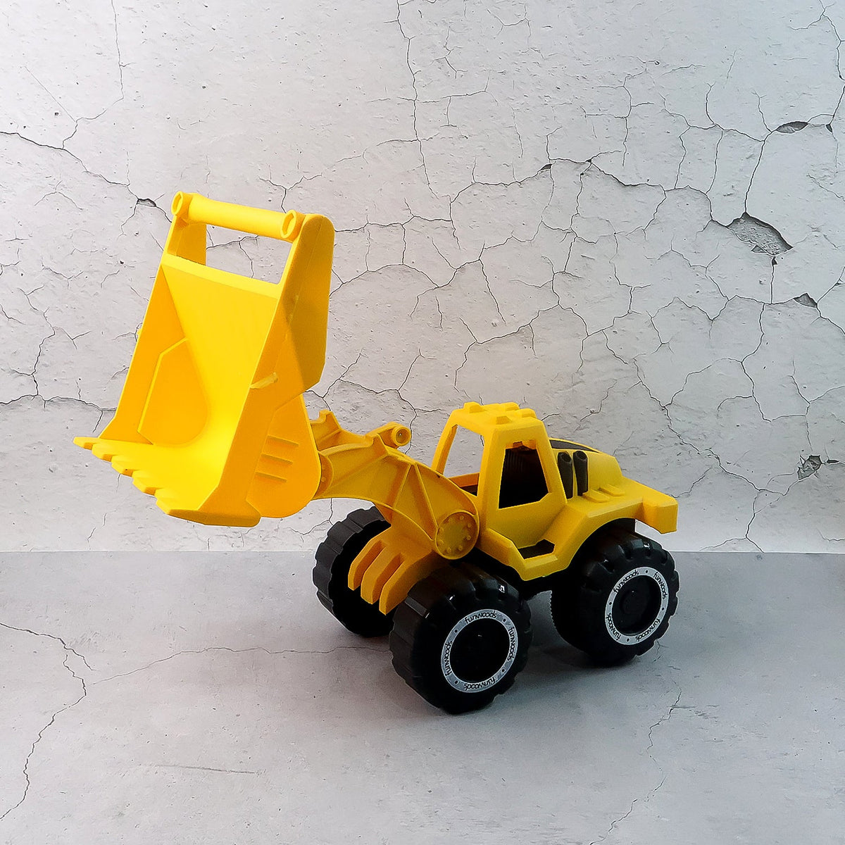 A yellow toy front-end loader with its scoop raised, set against a textured light gray wall.
