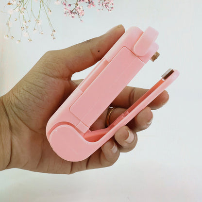 A hand holds the pink plastic bag sealer, showing its compact size and open sealing mechanism.