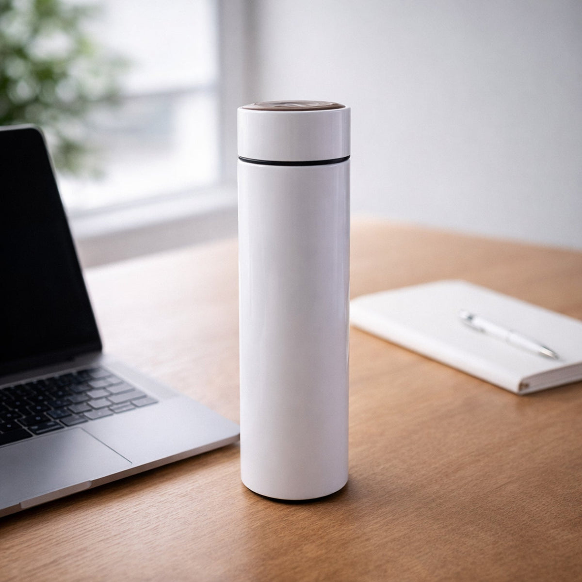 White thermal bottle standing on a wooden desk next to an open laptop and a white notebook.