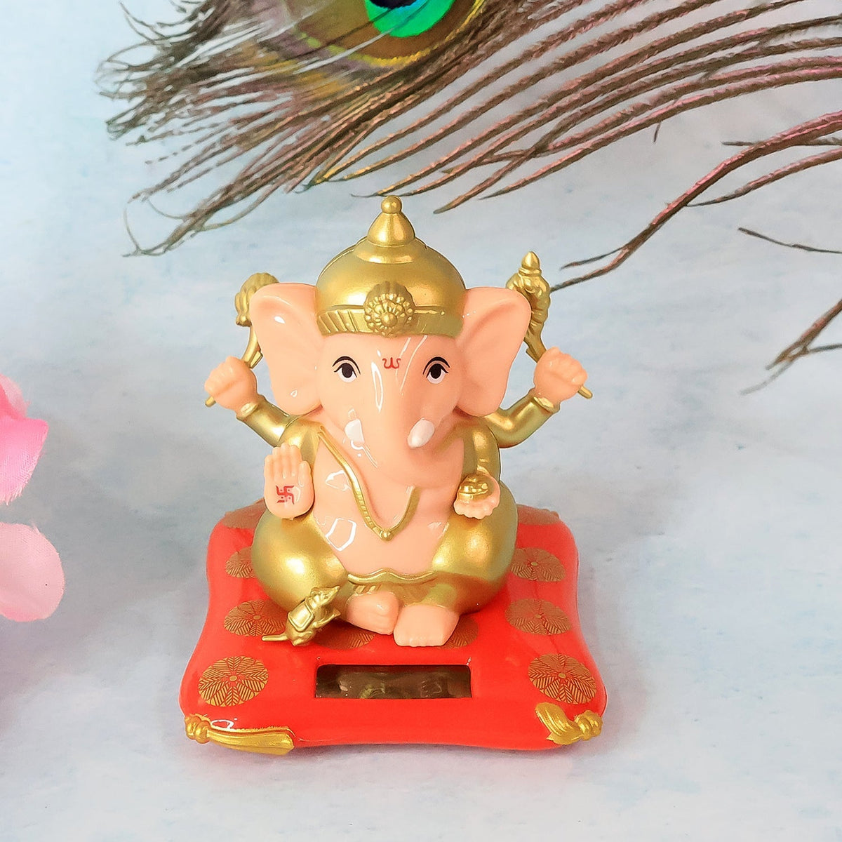 A Ganesha idol on a red base with gold accents, positioned in front of a peacock feather.