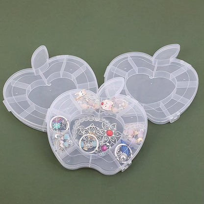 Three transparent apple-shaped organizer boxes are displayed on a dark green surface; the front box is open and filled with