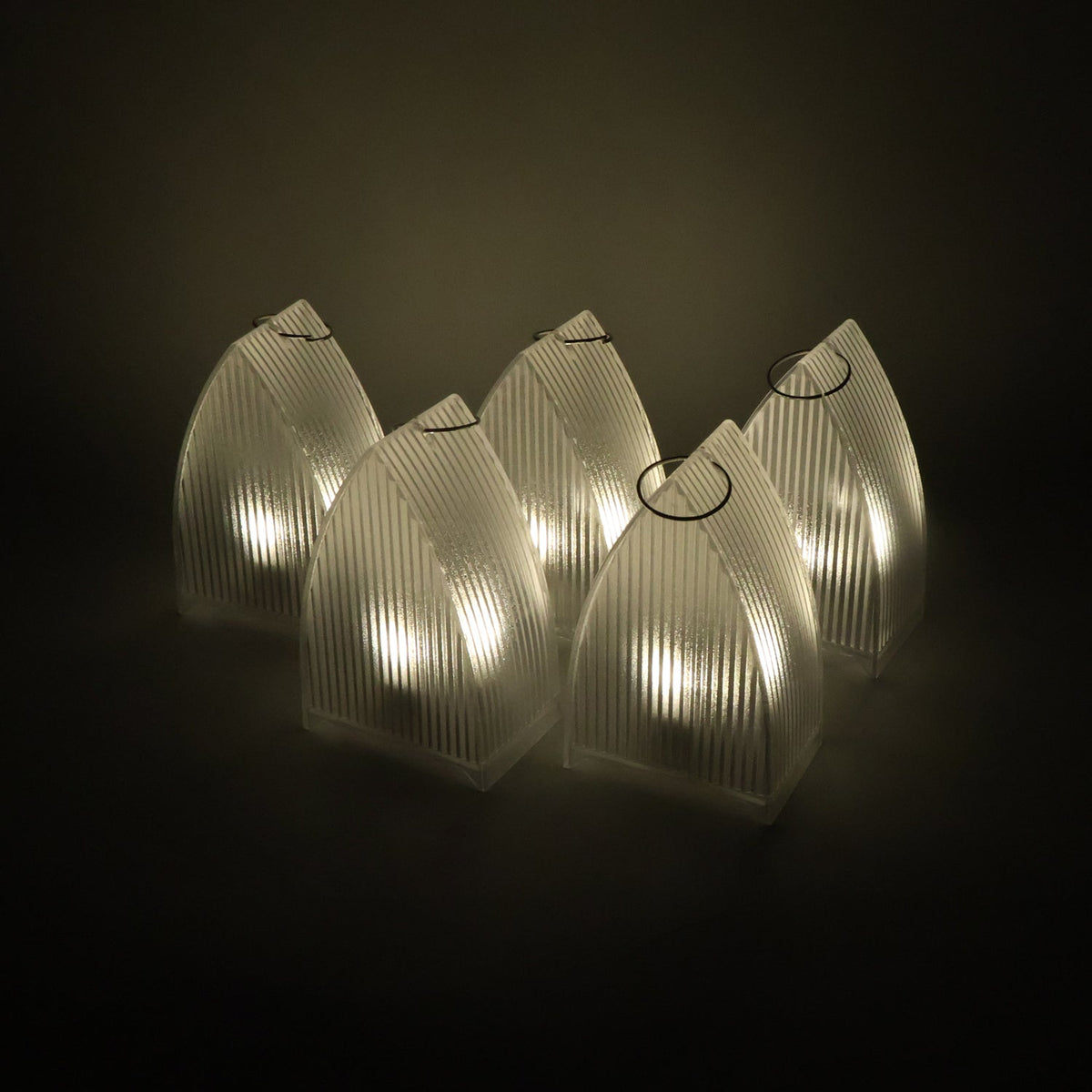 Five clear plastic ribbed lanterns with warm LED lights glowing in a dark setting.