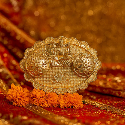 A gold-finished chopra with Ganesh and two ornate containers on a red and gold fabric, surrounded by orange marigold flowers.