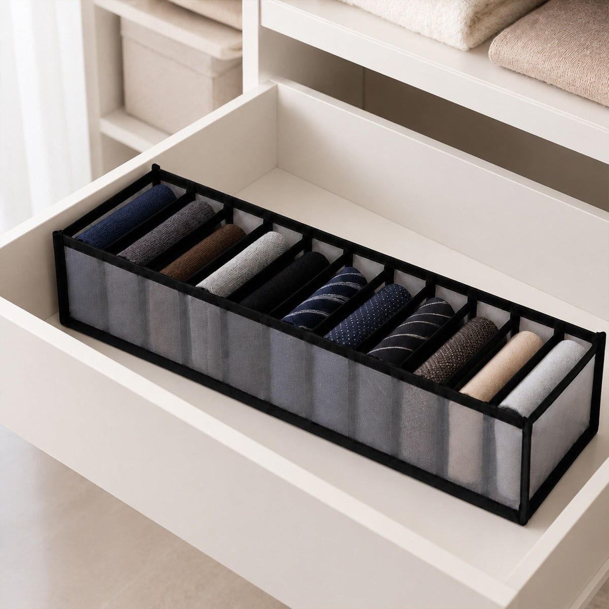 A gray 11-section fabric organizer filled with rolled ties and socks sits inside a white open drawer.