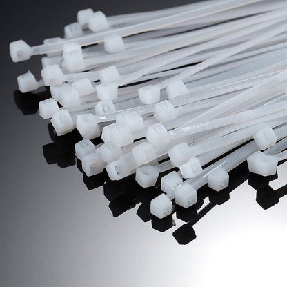 A close-up view of the interlocking heads of many white nylon cable ties on a reflective dark surface.