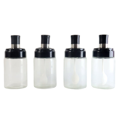 Four transparent spice jars with black lids and white spoons on a plain white background.
