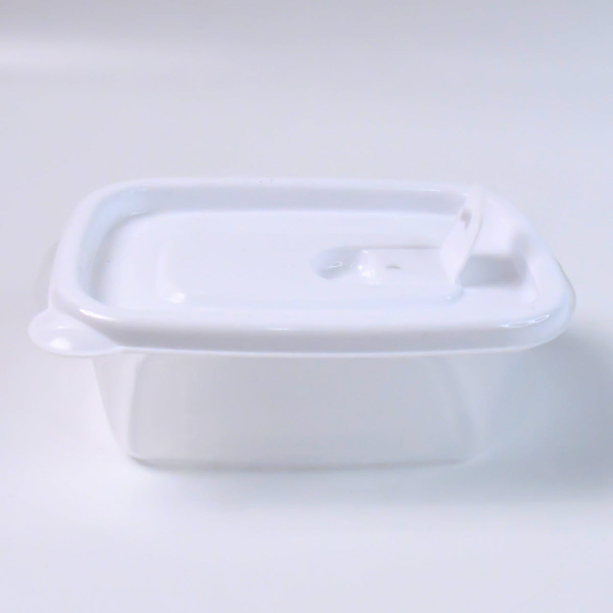 Side view of a single clear plastic food container with a white lid on a plain white background.