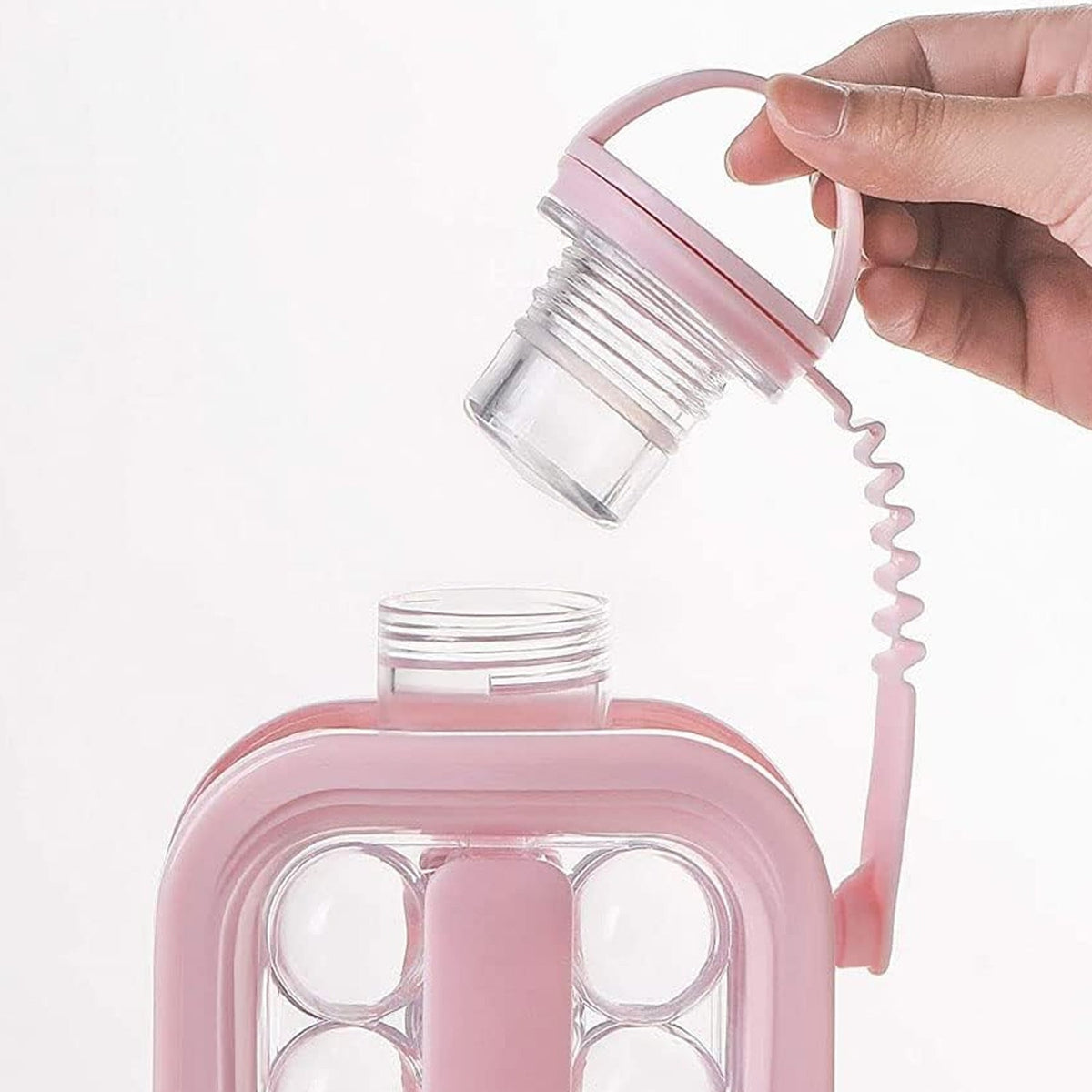 A hand holds the pink screw-top lid of an ice ball maker bottle, revealing the threaded opening and clear interior.