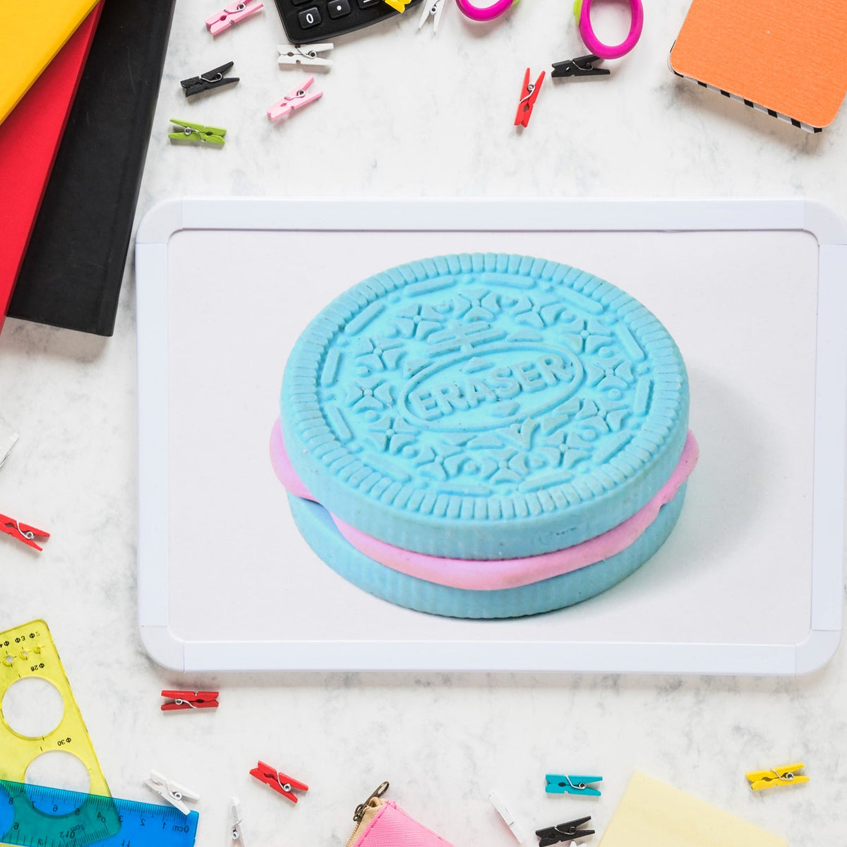 A large blue and pink cookie-shaped eraser is displayed on a small white dry-erase board with colorful clips around it.