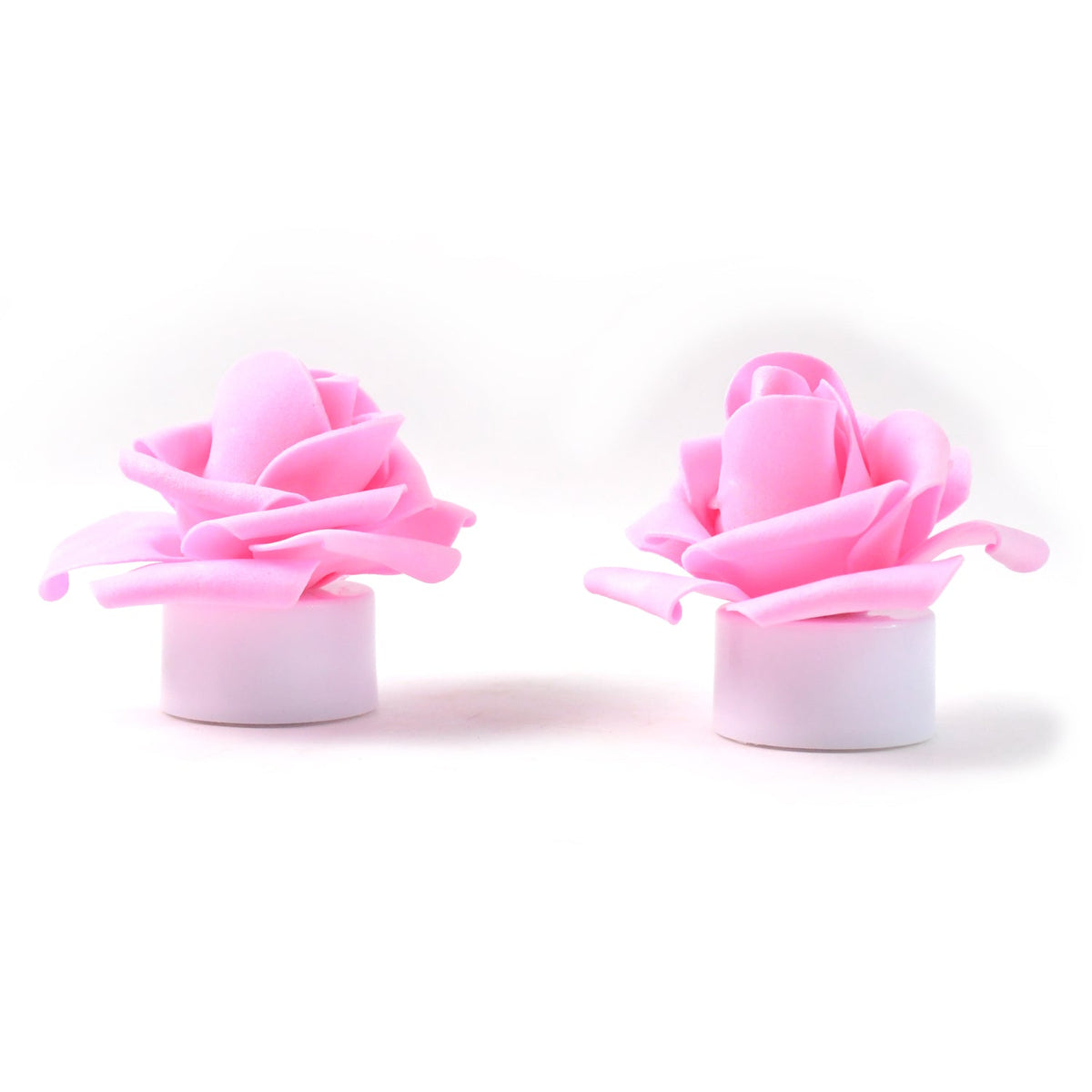 Two unlit pink rose tea lights with white bases on a plain white background.