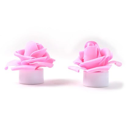 Two unlit pink rose tea lights with white bases on a plain white background.