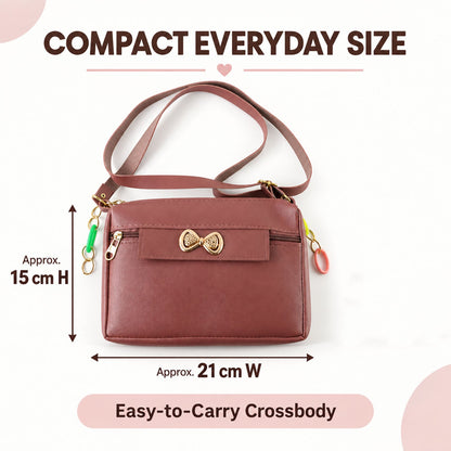 A mauve sling bag with a gold bow and colorful charms, showing approximate dimensions of 15cm H x 21cm W.