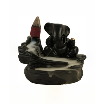 Black Ganesha smoke fountain with a lit incense cone and white smoke flowing down, presented against a plain white