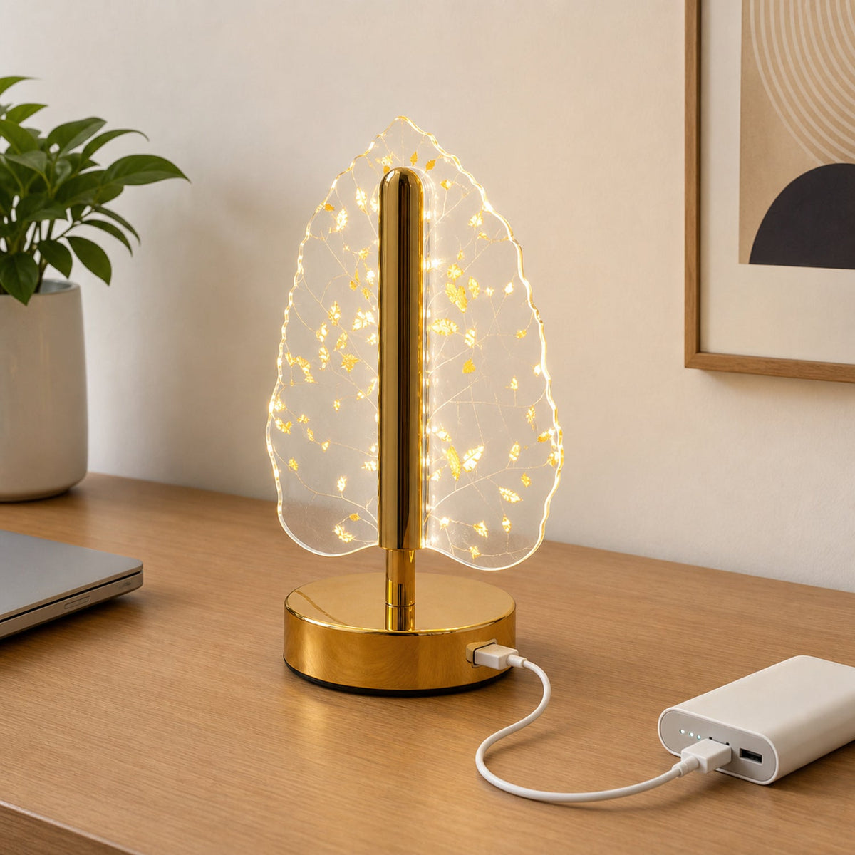 A golden crystal leaf LED table lamp on a wooden desk, connected to a white power bank via a USB cable.