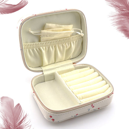 An open cherry print jewelry organizer case with empty compartments and a small pouch, surrounded by feathers.